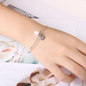 Elegant silver open bangle featuring a white pearl and polished heart charm on wrist