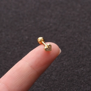 Macro shot of a golden heart stud earring with clear zircon inlay held on a fingertip