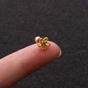 Close-up of golden flower stud earring with zircon and screw back on a fingertip