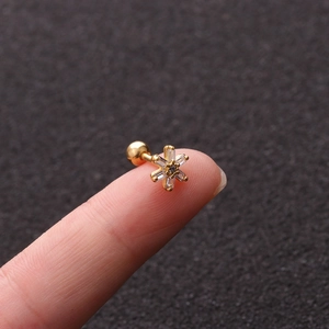 Macro shot of a gold star flower stud earring with clear zircon held on a fingertip
