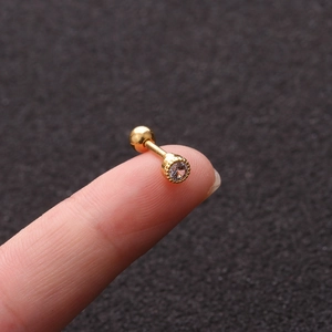 Macro shot of small gold screw back stud earring with clear zircon on a fingertip