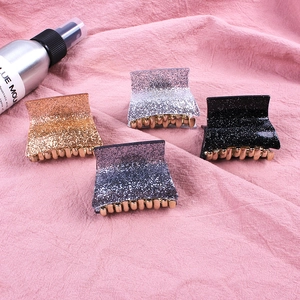 Detail view of four glitter acrylic hair claws in gold, silver, black and blue on pink fabric