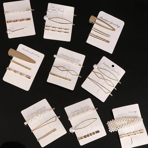 Detail of golden alloy hairpins and faux pearl clips set on a black reflective background