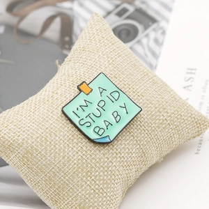 Detail of light green enamel pin shaped like a sticky note on beige linen background