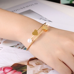 Elegant gold stainless steel heart and pearl charm bracelet worn with floral background