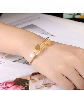 Detail of gold layered cuff bracelet with pearls, heart and clover charms on wrist