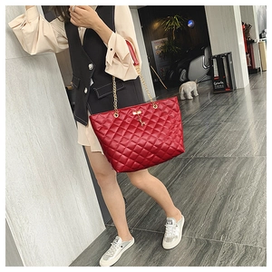 Close-up of red quilted tote bag with gold deer charm and chain shoulder strap detail