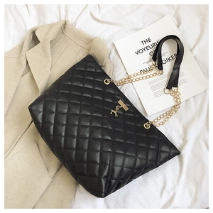 Detail of black quilted tote bag featuring golden chain strap and a small deer charm