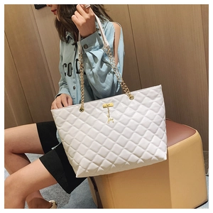 Detail view of a white quilted tote bag with golden chain strap and a deer charm accessory