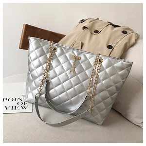 Close-up of silver quilted tote bag with gold chain strap and deer charm detail