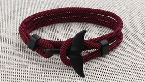 Macro detail of red woven rope bracelet with black whale tail charm and slider clasp