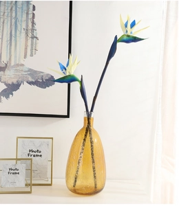 Artificial bird of paradise flowers with yellow petals in an amber glass vase decor