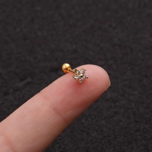Dettaglio macro di un piccolo orecchino a fiore dorato con zirconi sulla punta di un dito