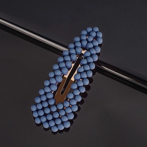 Detail of dark blue pearl hair clip with gold metal BB clip on reflective surface