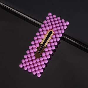 Detail of purple bead hair clip featuring rectangular metal base on reflective surface