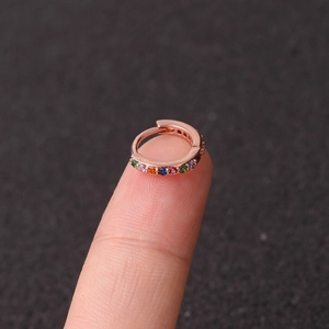 Close-up of mini rose gold zircon hoop earring with multicolored stones on a fingertip