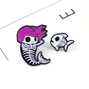 Detail view of skull mermaid enamel pin with purple hair and small fish bone brooch
