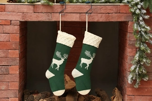 Detailed view of green knitted Christmas stockings with white reindeer hanging by a fireplace