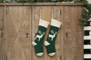 Detail of green knitted Christmas stockings with white reindeer hanging on a wood cabinet