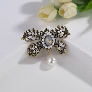 Vintage gold brooch with white pearls and dark rhinestones on a white wooden tray