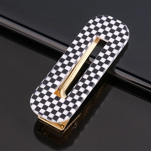 Detail of checkered acetate hair clip with golden metal base on a reflective surface