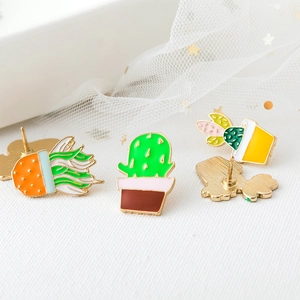 Three colorful enamel cactus brooches with gold metal edges on textured white fabric