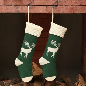 Pair of green knitted Christmas stockings with reindeer pattern hanging on brick fireplace