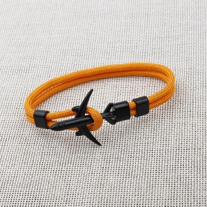 Detail of orange braided paracord bracelet featuring a black airplane clasp on white fabric