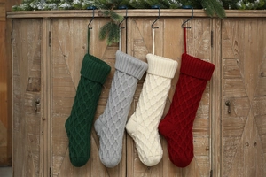 Große gestrickte Weihnachtssocken in vier Farben hängen an einem alten Holzschrankdekor