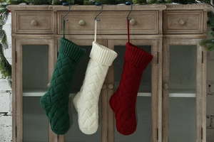 Detail of three knitted Christmas stockings in red, white and green with cable knit pattern