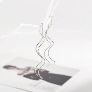 Elegant long S-shaped wavy silver threader earrings hanging on a white branch
