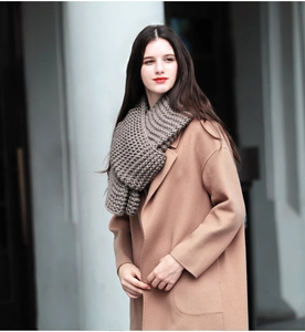 Detail view of a thick grey hand-knitted wool scarf styled with a classic camel coat
