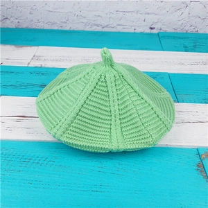 Mint green cable knit beret with ribbed texture and top stem on blue wood background