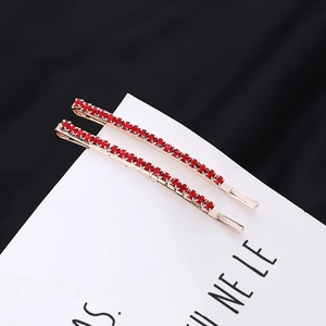 Detailed view of two gold-plated hair clips with sparkling red rhinestones on a card