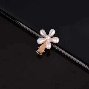 Close-up of golden floral hair clip with inlaid white pearls on a reflective black base