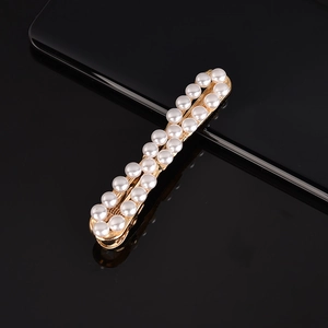Detail shot of golden metal hair pin with two rows of white pearls on a black surface
