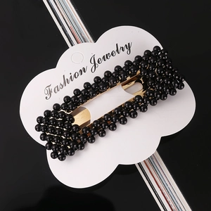 Detail of black pearl hair clip with gold metal base on a white cloud display card