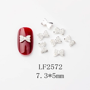 Détail de bijoux d'ongles nœuds avec perles blanches et base argentée sur ongles rouges