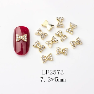 Vue macro de bijoux d'ongles nœuds dorés 7,3x5mm avec strass sur manucure rouge