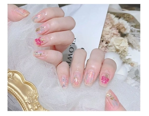 Detail of pink nail art with dried flowers, gold foil, and glitter on lace background
