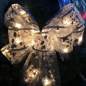 Detail of white glowing LED Christmas bow with black star patterns on a green tree