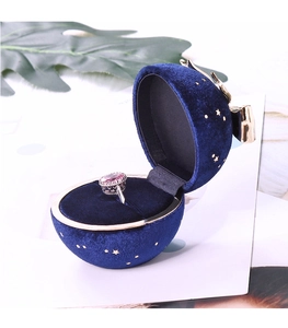 Macro detail of navy velvet sphere ring box with gold stars and elegant bow accent