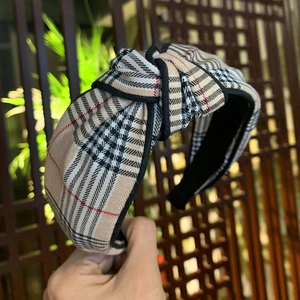 Detailed close-up of wide-brimmed beige plaid knotted headband with black fabric trim