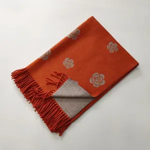 Detail of orange cashmere scarf with grey camellia jacquard and handmade tassel trim