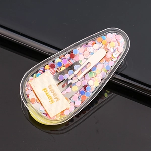 Macro detail of a colorful sequin hair clip with a handmade label on a sleek black surface