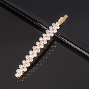 Macro view of gold-tone hair clip with double rows of miniature pearls on black background