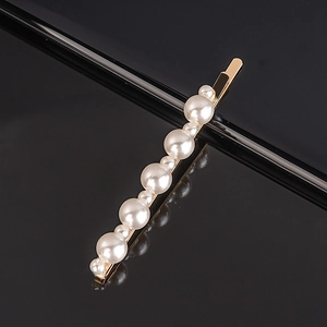 Detailed view of golden hair clip with alternating pearls on reflective black background