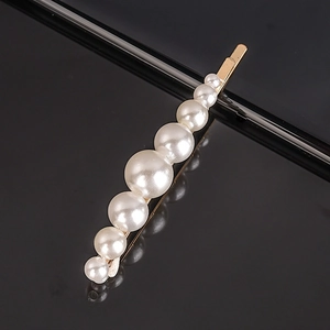 Detail shot of 7 white pearls set on a gold-plated metal hair clip over black surface