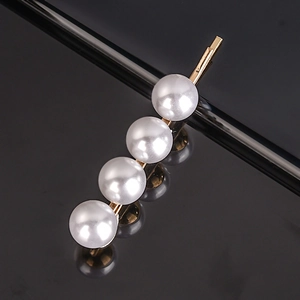 Macro shot of gold hair clip featuring four polished white pearls on a black background