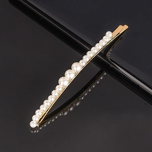 Close-up of golden metal hair clip featuring gradient white pearls on black surface